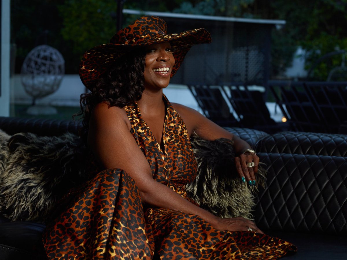 Woman in leopard print dress and cowboy hat sitting on couch with feathered cushion