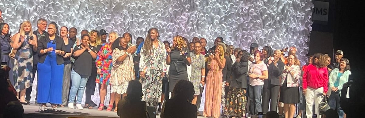 Large group of people standing on stage together in formal attire against a sparkly backdrop